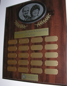 A commemorative wooden plaque featuring a portrait of a couple, with spaces for scholarship recipients' names in business, affiliated with a university.