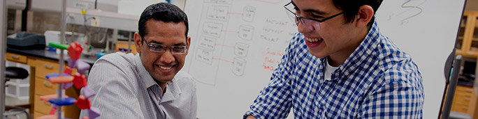 A professor and a student in a classroom attentively observing a whiteboard filled with educational content.