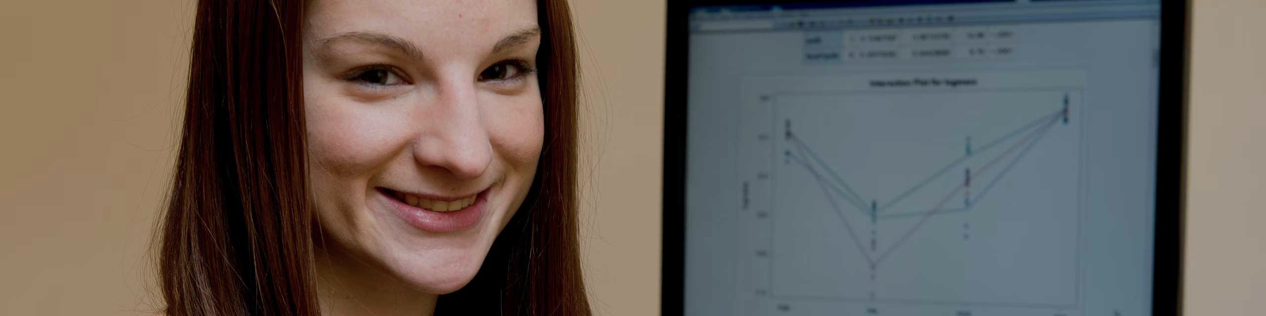 Person smiling with a computer monitor in the background displaying a line graph.