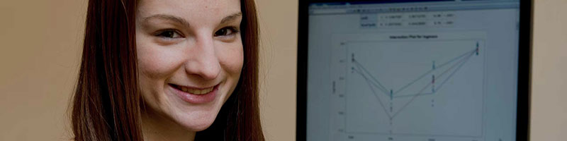 Person smiling with a computer monitor in the background displaying a line graph.
