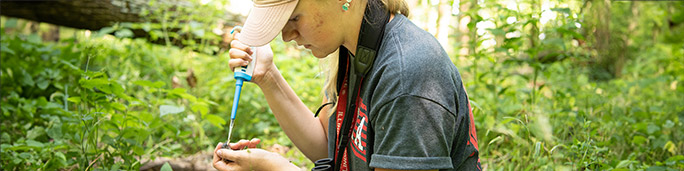 A student in a fieldtrip gently cradles a tiny animal in her hand.