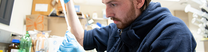 A student in a lab coat performing experiments in a research facility.